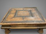 une vieille table basse en bois dont le plateau est orné d'un motif décoratif