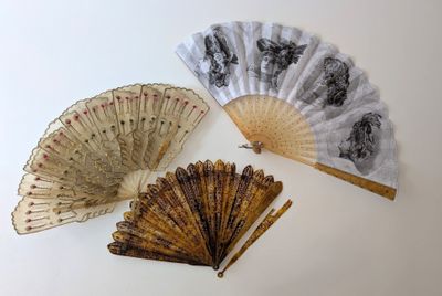 Trois vieux ventilateurs sont posés sur une surface blanche ; l'un est ouvert et l'autre fermé.