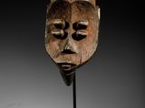 un gros plan d'un masque en bois posé sur un socle, sur une surface blanche