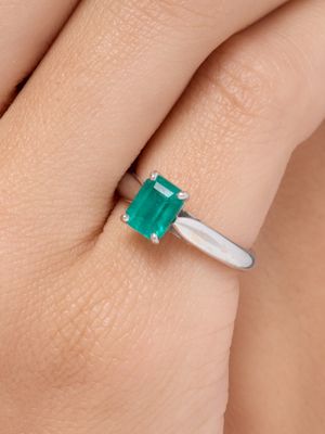 un gros plan sur la main d'une femme tenant une bague en émeraude