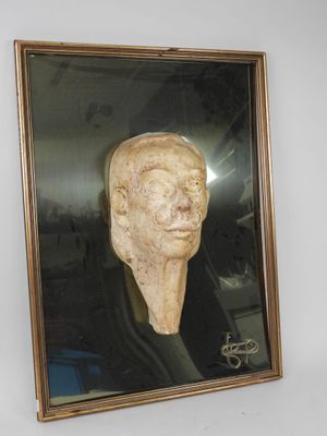 tableau représentant la tête d'un homme, dans un cadre doré, accroché à un mur blanc