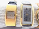 three different watches on a white cloth with a gold band