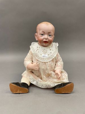 une poupée ancienne en porcelaine représentant un bébé assis par terre