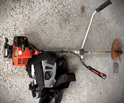 a close up of a string trimmer on the ground next to a pair of gloves and a pair of scissors