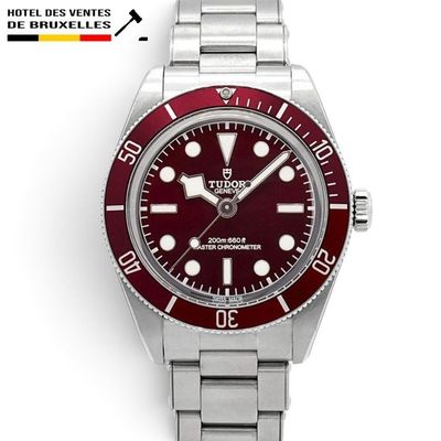a close up of a watch with a red dial on a bracelet