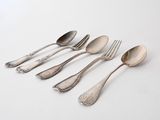 six spoons and a fork are lined up on a white surface
