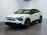 La voiture blanche est garée dans une grande pièce équipée d'un ventilateur de plafond.