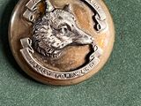 un badge en métal sur lequel est représenté un loup