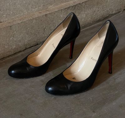 une paire de chaussures à talons hauts noires posées sur un sol en béton, près du mur