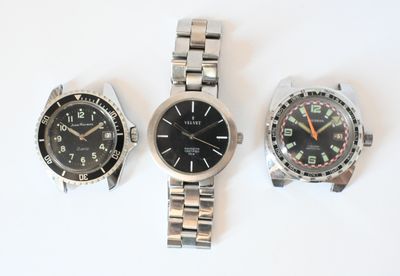 three watches are sitting on a white surface, one is black and the other is silver