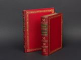 an old red book with gold trim sitting on top of a black surface