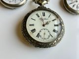 three antique pocket watches sitting on a white surface