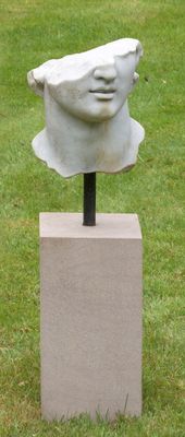 sculpture représentant la tête d'une femme, posée sur un socle dans un espace vert