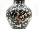un vase noir avec un couvercle vert sur lequel est représenté un arbre
