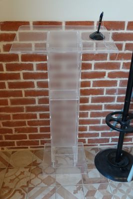 a clear podium with a black chair and a brick wall in the background