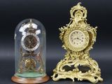 deux horloges posées sur une table, sous un dôme en verre