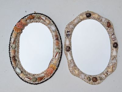 two oval mirrors with shells on them on a table