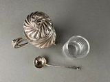 a silver tea strainer and a glass of water on a table