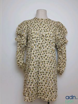 une robe blanche ornée de fleurs jaunes, posée sur un présentoir pour mannequin