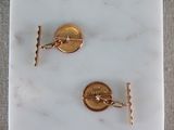 two gold cufflinks with a coin on a marble plate