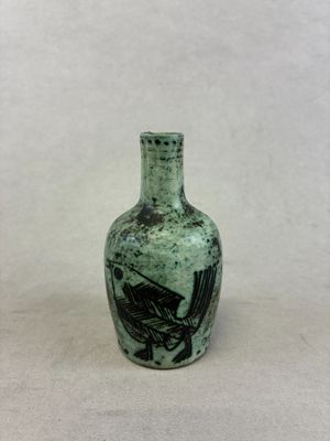 un vase vert avec un oiseau posé sur une table