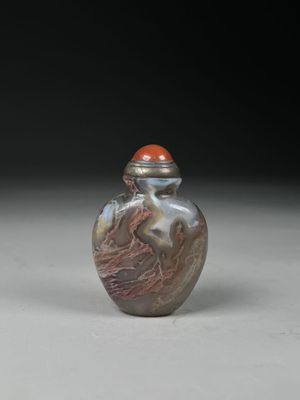 une image représentant une fiole à tabac en verre argenté et rouge posée sur une surface blanche
