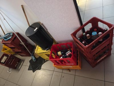 Plusieurs caisses de bière sont alignées par terre, à côté d'une poubelle