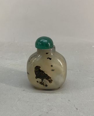 une petite bouteille en verre avec un bouchon vert posée sur une surface blanche