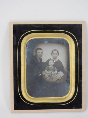 portrait of a man and woman holding a baby in a black and gold frame