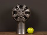 a metal sculpture of a sun face next to an apple on a table