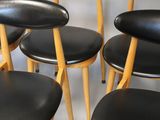 six black leather stools with wooden legs are arranged in a circle