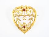 une broche en or en forme de cœur, ornée d'une pierre rouge entourée de feuilles