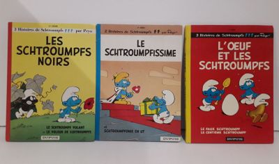 Trois livres sur les Schtroumpfs sont alignés sur une surface blanche