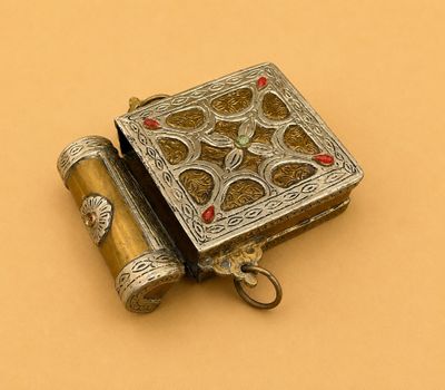 une vieille boîte en argent contenant une pierre rouge posée sur un fond jaune