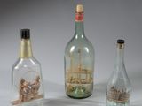 three glass bottles with a ship in them on a white surface