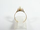 a white pearl and gold ring on a clear stand