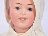 a close up of a doll wearing a white dress and a bonnet