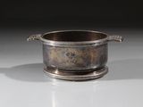 une tasse en argent avec une anse, posée sur une table blanche