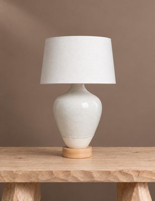 une lampe de table blanche posée sur une table en bois, près d'un mur marron