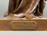 bronze statue of a woman sitting on a bench with her hands on her knees