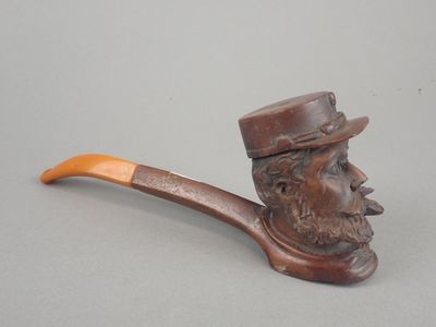 une pipe sur laquelle est représenté un visage d'homme et un porte-pipe en bois