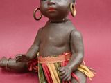 doll of a baby sitting on a pink surface with a pair of earrings