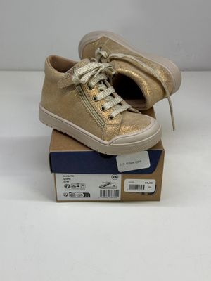 Les baskets dorées sont posées sur une boîte en carton.