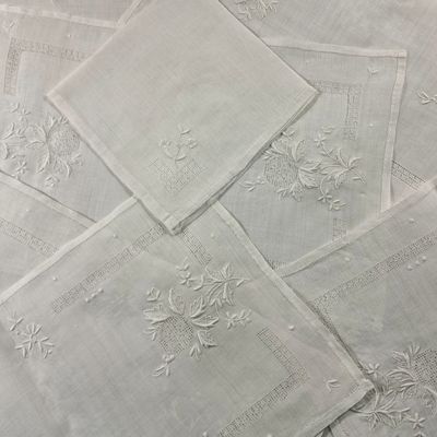plusieurs serviettes de table en lin blanc ornées de fleurs brodées, posées sur une table