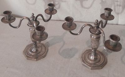 deux chandeliers en argent posés sur une table, avec un mur blanc en arrière-plan