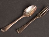 two silver spoons and a fork on a black surface