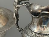 a silver pitcher sitting next to a bowl on a table