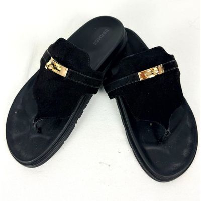une paire de pantoufles noires ornées de boucles dorées sur un fond blanc