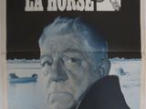 une vieille affiche de cinéma représentant un homme en manteau noir qui fixe l'objectif