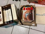 de nombreux livres dans une boîte posée par terre, à côté d'un appareil photo